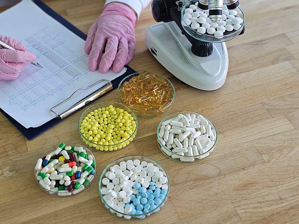 Nhân viên phòng thí nghiệm kiểm tra nhiều dạng thuốc bên cạnh kính hiển vi và hồ sơ